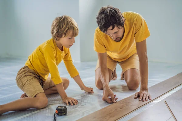 Ojciec i syn, instalowanie nowych drewnianych podłóg laminowanych na piętrze ciepły film. podczerwień system pod podłogi laminowane ogrzewania podłogowego — Zdjęcie stockowe