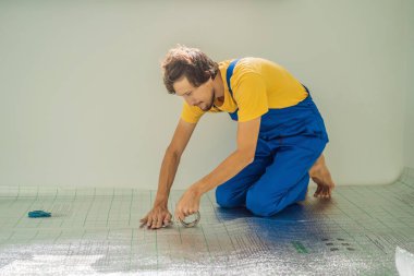 Üstat odaya üstüste binen termal yalıtımı kuruyor. Zemin ısıtma sistemi. Erkek el güçlendirilmiş bant tutuyor. Dairenin tamiri, yer yalıtımı.