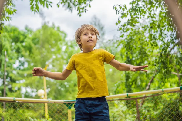 Menino feliz joga ao ar livre no jardim pulando alto no céu em trampolim — Fotografia de Stock