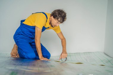 Üstat odaya üstüste binen termal yalıtımı kuruyor. Zemin ısıtma sistemi. Erkek el güçlendirilmiş bant tutuyor. Dairenin tamiri, yer yalıtımı.