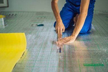 Üstat odaya üstüste binen termal yalıtımı kuruyor. Zemin ısıtma sistemi. Erkek el güçlendirilmiş bant tutuyor. Dairenin tamiri, yer yalıtımı.