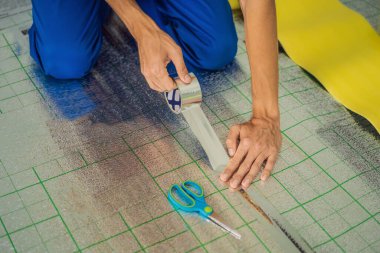 Üstat odaya üstüste binen termal yalıtımı kuruyor. Zemin ısıtma sistemi. Erkek el güçlendirilmiş bant tutuyor. Dairenin tamiri, yer yalıtımı.