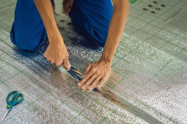 Üstat odaya üstüste binen termal yalıtımı kuruyor. Zemin ısıtma sistemi. Erkek el güçlendirilmiş bant tutuyor. Dairenin tamiri, yer yalıtımı.