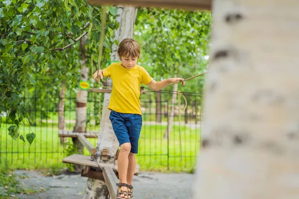 Um rapazinho num parque de cordas. Recreação física ativa da criança ao ar livre no parque. Treinamento para crianças — Fotografia de Stock