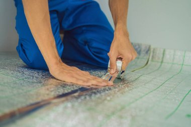 Üstat odaya üstüste binen termal yalıtımı kuruyor. Zemin ısıtma sistemi. Erkek el güçlendirilmiş bant tutuyor. Dairenin tamiri, yer yalıtımı.