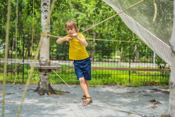 Un niño en un parque de cuerdas. Recreación física activa del niño al aire libre en el parque. Formación para niños — Foto de Stock