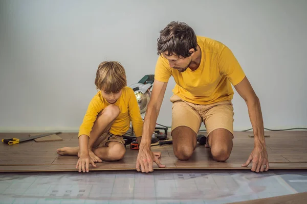 Otec a syn instalace nové dřevěné laminátové podlahy v patře teplého filmu. infračervený systém podlahového vytápění pod laminátové podlahy — Stock fotografie