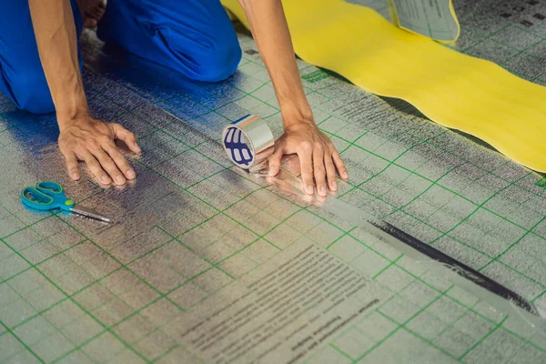 Üstat odaya üstüste binen termal yalıtımı kuruyor. Zemin ısıtma sistemi. Erkek el güçlendirilmiş bant tutuyor. Dairenin tamiri, yer yalıtımı.