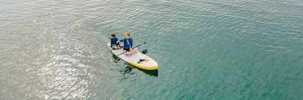 Μητέρα και γιος κωπηλασία επί του σκάφους σταθεί διασκεδάζοντας κατά τη διάρκεια των καλοκαιρινών διακοπές στην παραλία BANNER, LONG FORMAT — Φωτογραφία Αρχείου