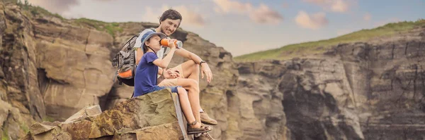 BANNER, FORMATO LUNGO Papà e figlio turisti sullo sfondo di belle rocce e il mare. Concetto escursionistico. Mantella di Tobizin. Vladivostok, isola Russky. Mare del Giappone. Primorye. Primorsky krai. Natura di — Foto Stock