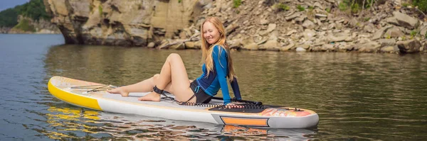 BANNER, LONGO FORMATO Jovens mulheres se divertindo se levantam remo no mar. SUP. Menina de cabelo vermelho Treinamento em Paddle Board perto das rochas — Fotografia de Stock