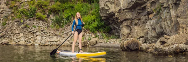 BANNER, LANG FORMAT Jonge vrouwen die plezier hebben staan te peddelen in de zee. Een SUP. Rood haar meisje training op peddel boord in de buurt van de rotsen — Stockfoto