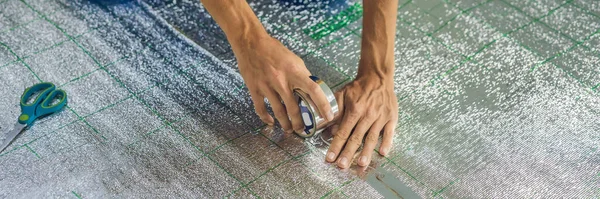 BANNER, LONG FORMAT Master installeert de overlappende warmte-isolatie in de ruimte. Vloerverwarmingsinstallatie. Mannelijke hand houdt versterkte tape vast. Reparatie in het appartement, isolatie — Stockfoto