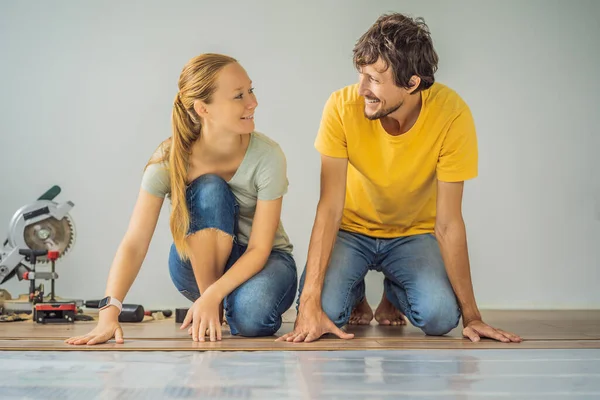 Pareja casada instalando nuevos pisos laminados de madera en un piso de película caliente. Sistema de calefacción por suelo radiante infrarrojo bajo suelo laminado —  Fotos de Stock