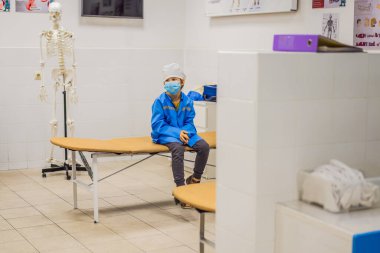 Hastane içinde doktor üniformasıyla doktorculuk oynayan çocuk.