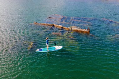 Kürek çeken bir kadın, terk edilmiş kırık bir gemi enkazının yanında yemek.