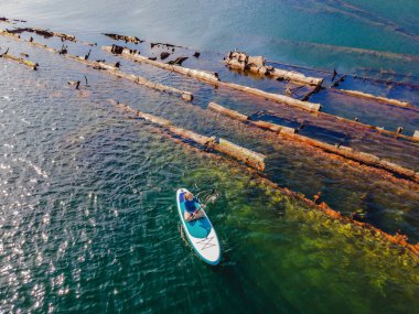Kürek çeken bir kadın, terk edilmiş kırık bir gemi enkazının yanında yemek.
