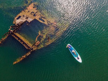 Kürek çeken bir kadın, terk edilmiş kırık bir gemi enkazının yanında yemek.