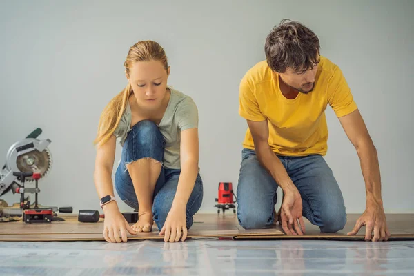 Coppia sposata l'installazione di nuovi pavimenti in laminato di legno su un pavimento caldo pellicola. Sistema di riscaldamento a pavimento a infrarossi sotto pavimento in laminato — Foto Stock