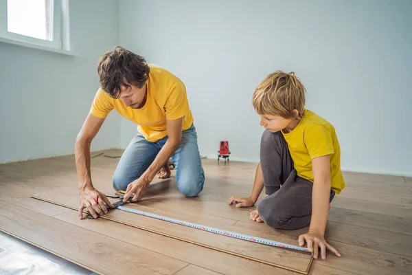 Ojciec i syn, instalowanie nowych drewnianych podłóg laminowanych na piętrze ciepły film. podczerwień system pod podłogi laminowane ogrzewania podłogowego — Zdjęcie stockowe