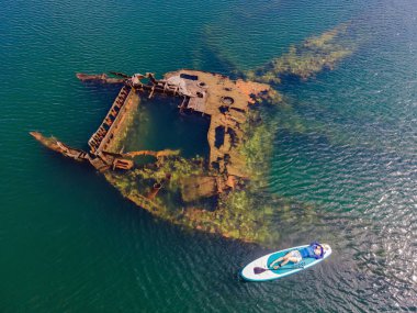 Kürek çeken bir kadın, terk edilmiş kırık bir gemi enkazının yanında yemek.