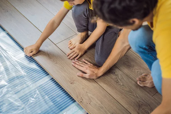 Father and son installing new wooden laminate flooring on a warm film floor. Infrared floor heating system under laminate floor — Stock Photo, Image