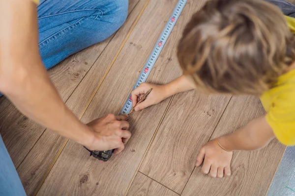 Padre e hijo instalando nuevos pisos laminados de madera en un piso de película caliente. sistema de calefacción por suelo radiante infrarrojo bajo suelo laminado — Foto de Stock