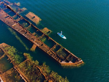 Kürek çeken bir kadın, terk edilmiş kırık bir gemi enkazının yanında yemek.