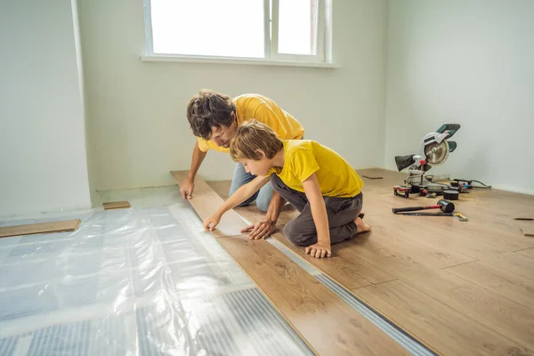 Padre e figlio l'installazione di nuovi pavimenti in laminato di legno su un pavimento caldo pellicola. sistema di riscaldamento a pavimento a infrarossi sotto pavimento in laminato — Foto Stock