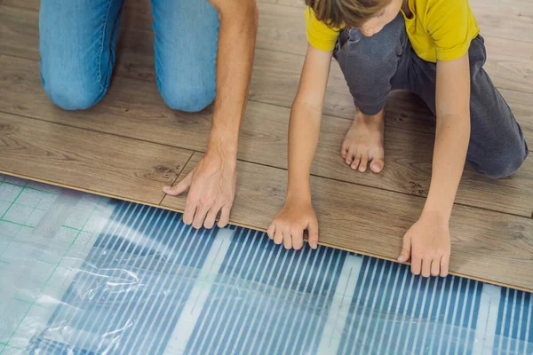 Padre e figlio l'installazione di nuovi pavimenti in laminato di legno su un pavimento caldo pellicola. sistema di riscaldamento a pavimento a infrarossi sotto pavimento in laminato — Foto Stock