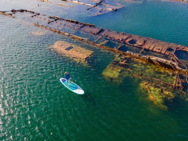 Kürek çeken bir kadın, terk edilmiş kırık bir gemi enkazının yanında yemek.