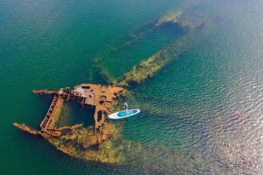 Kürek çeken bir kadın, terk edilmiş kırık bir gemi enkazının yanında yemek.