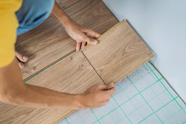 男人在温馨的片子的地板上安装新的木地板。红外地板采暖系统下强化地板 — 图库照片