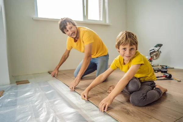 Padre e figlio l'installazione di nuovi pavimenti in laminato di legno su un pavimento caldo pellicola. sistema di riscaldamento a pavimento a infrarossi sotto pavimento in laminato — Foto Stock