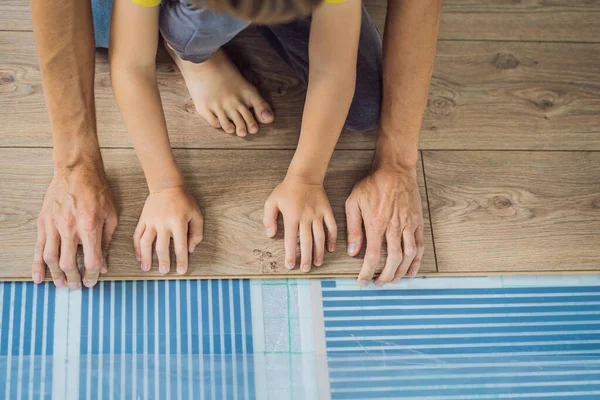 Padre e figlio l'installazione di nuovi pavimenti in laminato di legno su un pavimento caldo pellicola. sistema di riscaldamento a pavimento a infrarossi sotto pavimento in laminato — Foto Stock