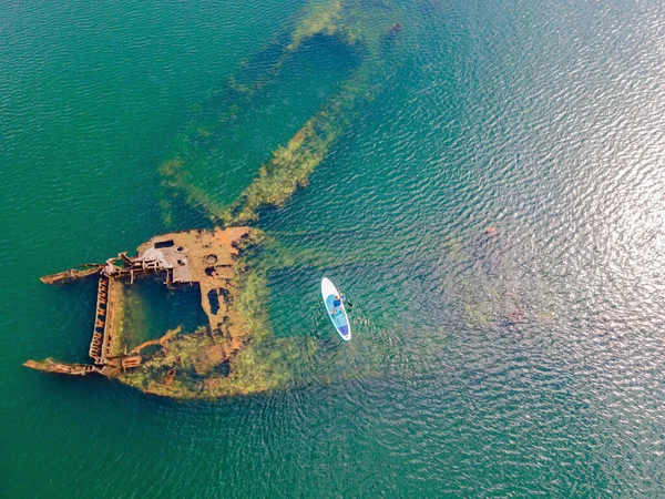 Kürek çeken bir kadın, terk edilmiş kırık bir gemi enkazının yanında yemek.