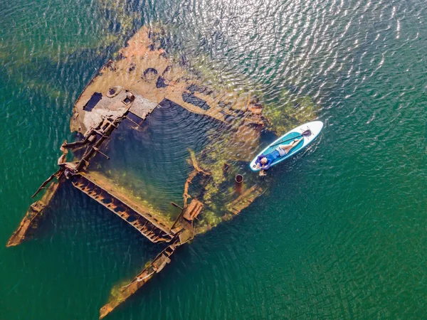 Kürek çeken bir kadın, terk edilmiş kırık bir gemi enkazının yanında yemek.