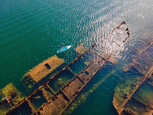 Kürek çeken bir kadın, terk edilmiş kırık bir gemi enkazının yanında yemek.
