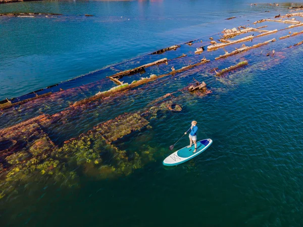 Mulher a bordo, jantar ao lado de um naufrágio abandonado a sair do mar. — Fotografia de Stock