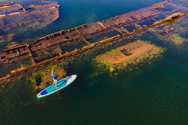 Kürek çeken bir kadın, terk edilmiş kırık bir gemi enkazının yanında yemek.