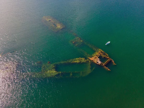 Kürek çeken bir kadın, terk edilmiş kırık bir gemi enkazının yanında yemek.