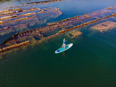 Kürek çeken bir kadın, terk edilmiş kırık bir gemi enkazının yanında yemek.