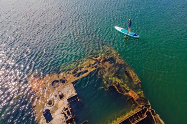 Kürek çeken bir kadın, terk edilmiş kırık bir gemi enkazının yanında yemek.