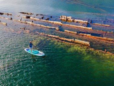 Kürek çeken bir kadın, terk edilmiş kırık bir gemi enkazının yanında yemek.