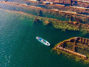 Kürek çeken bir kadın, terk edilmiş kırık bir gemi enkazının yanında yemek.