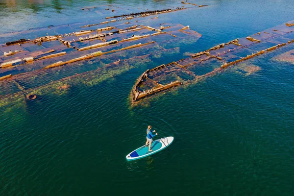Femme sur la planche à pagaie, soup à côté de naufrage cassé abandonné sortant de la mer — Photo