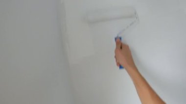 Pov atışı. Bir adam boya silindiri kullanarak duvar boyuyor.
