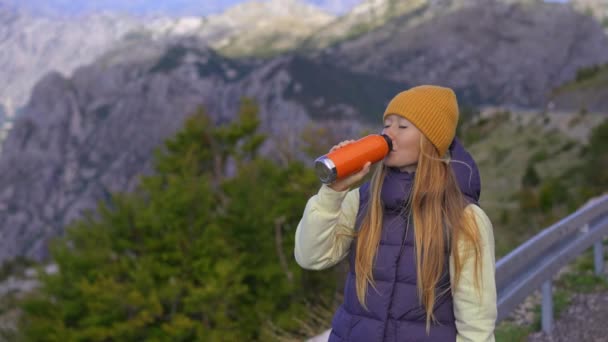 Жінка їде в гори. Вона п'є гарячий напій з оранжевого кольору термос — стокове відео