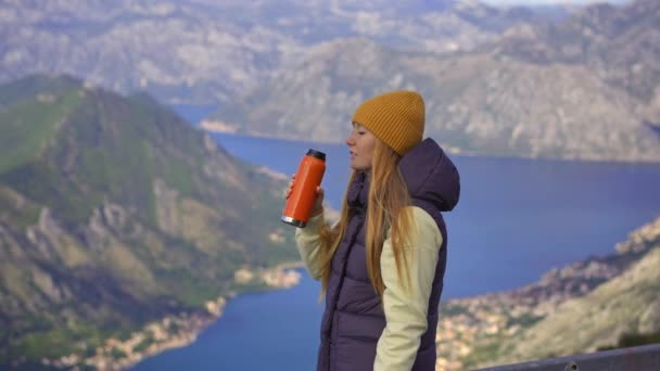 Μια γυναίκα ταξιδεύει στο Μαυροβούνιο το φθινόπωρο. Πίνει ένα ζεστό ρόφημα από ένα θερμός με τον κόλπο Μπόκα Κοτόρσκα σε φόντο — Αρχείο Βίντεο