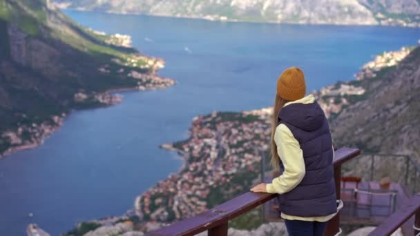 Una mujer viaja a Montenegro en otoño. Ella mira la bahía de Boka Kotorska desde un punto de vista en una montaña — Vídeos de Stock